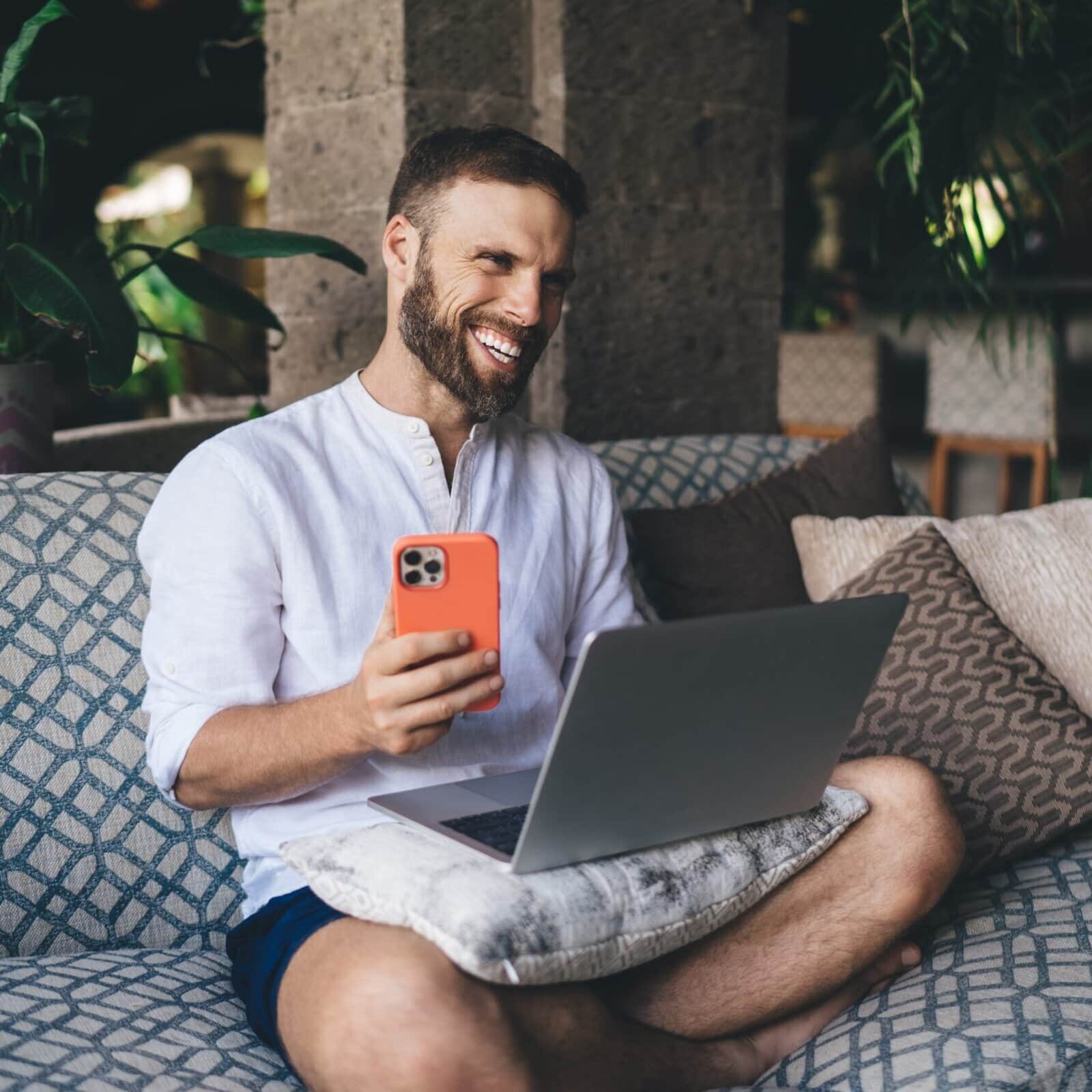 Happy,Freelancer,Holding,Smartphone,While,Working,On,Laptop,,Laughing,During
