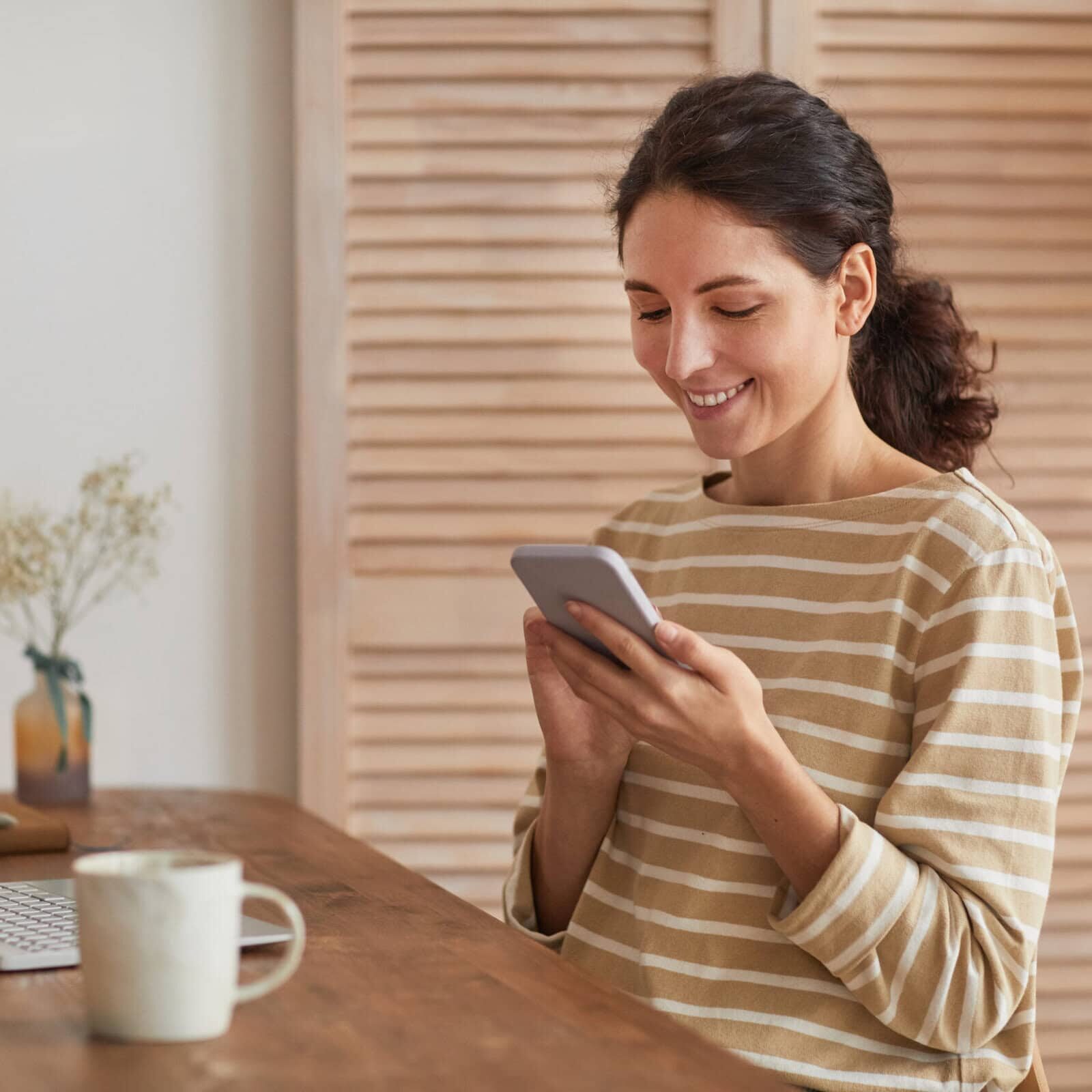 Warm,Toned,Portrait,Of,Smiling,Young,Woman,Using,Smartphone,At