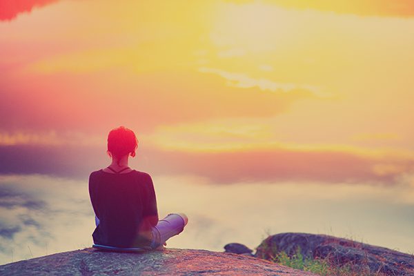 woman sitting on the edge of a mountain looking out at a sunrise