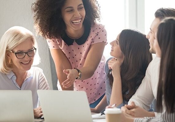 five people meeting and engaged in conversation in front of two laptops